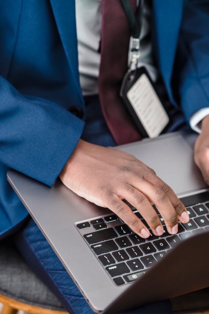 Close-up of a businessman in a blue suit working on a laptop indoors.